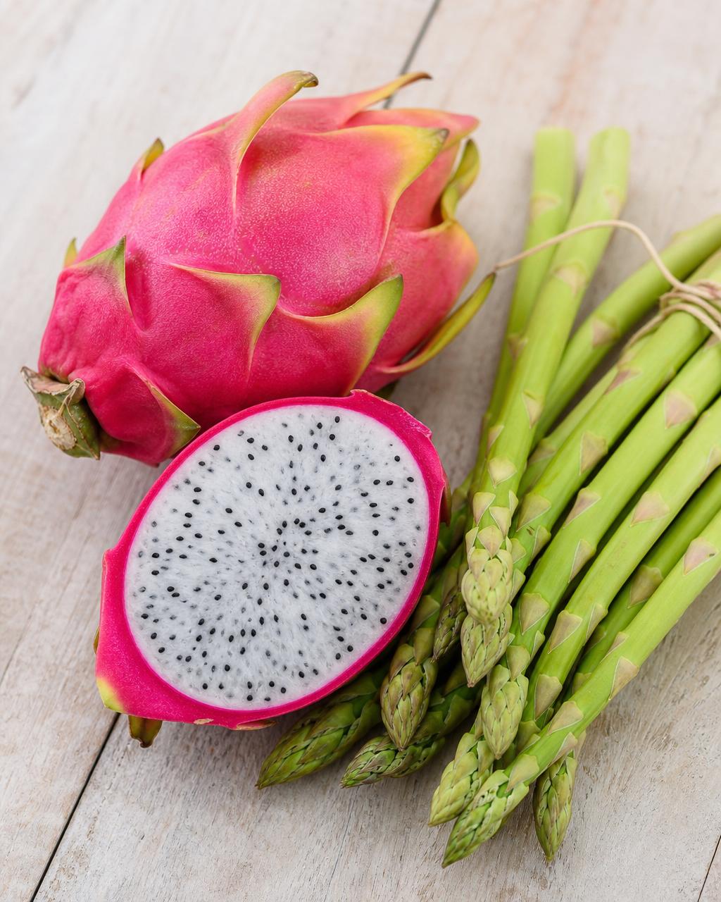 Whole and halved pink dragon fruit with a bundle of fresh green asparagus spears